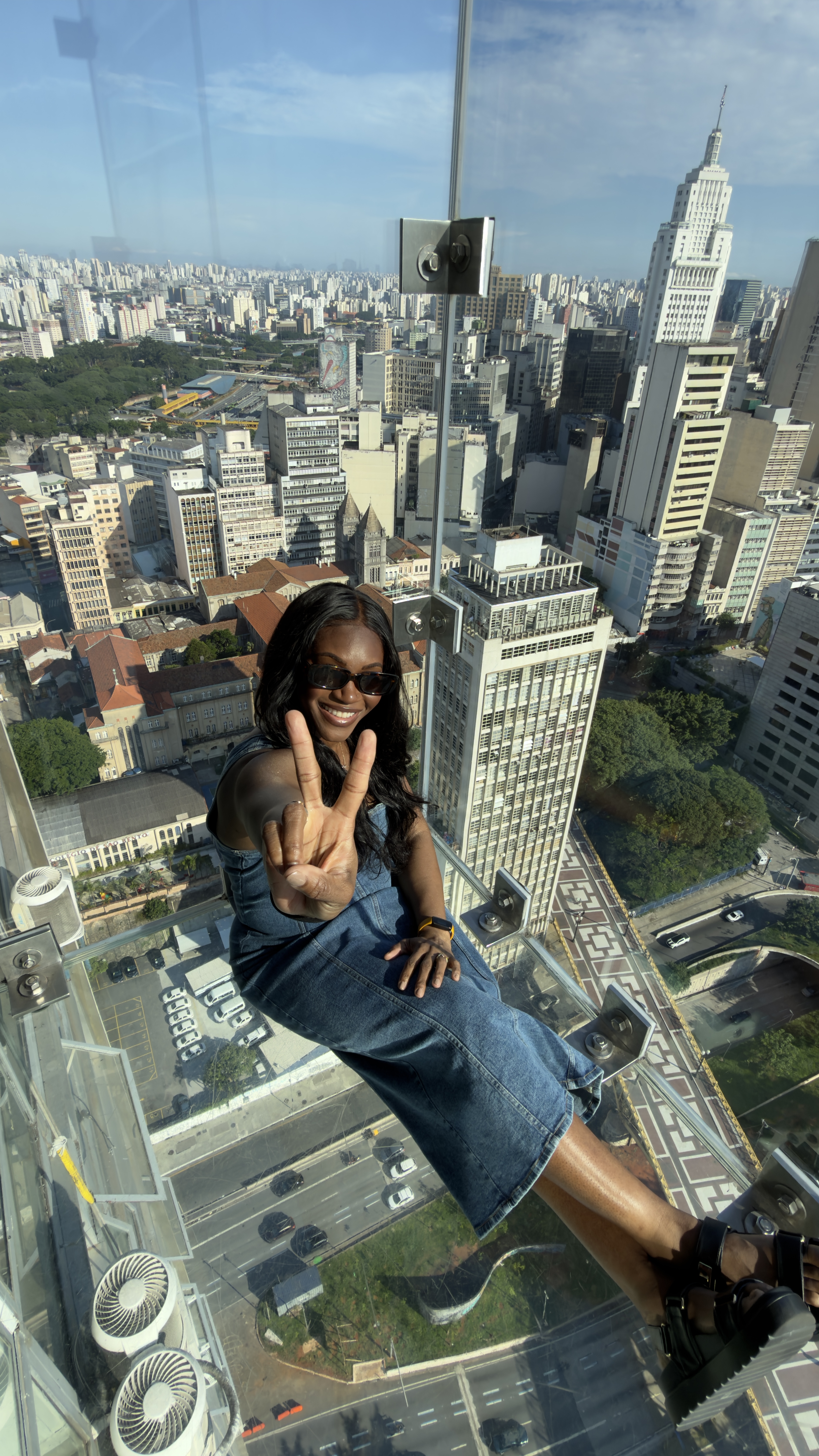 Raina on a glass floor skyscraper overlooking São Paulo